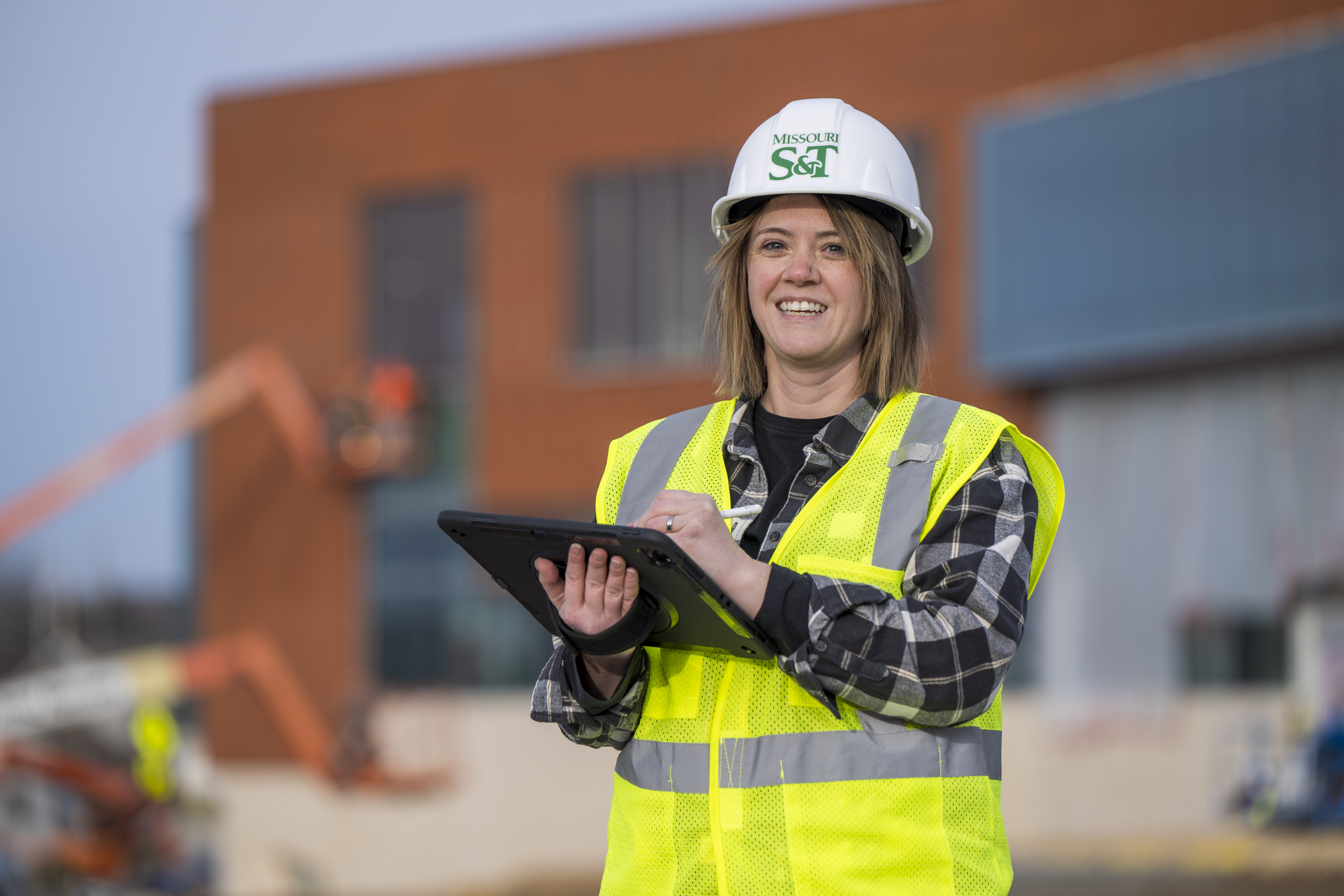 Sarah, a student at Missouri S&T, has a safety vest and Missouri S&T construction helmet while writing on an iPad